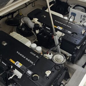 Boat engine compartment with two black Volvo Penta engines, hoses, gauges, and maintenance access hatches visible in a white fiberglass bay.